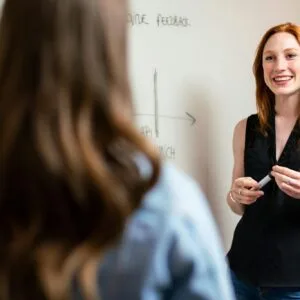 Two women discussing and planning a project in an office setting using a whiteboard.